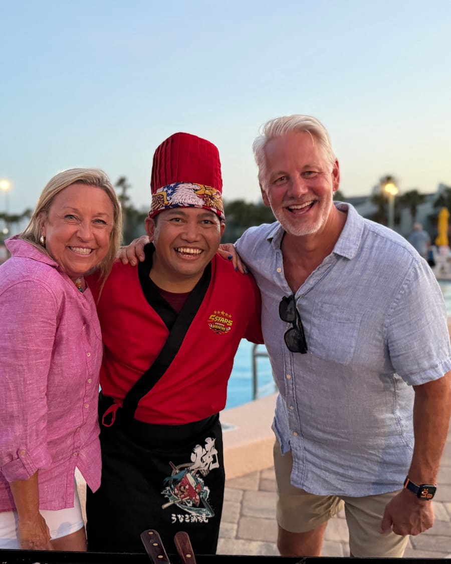 The chef standing between two guests at a poolside booking at dusk