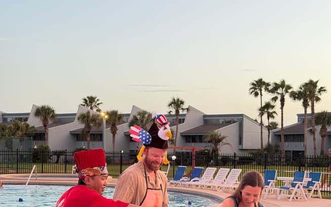 Chef cooking on the flat-top while two guests in novelty hats watch from the poolside