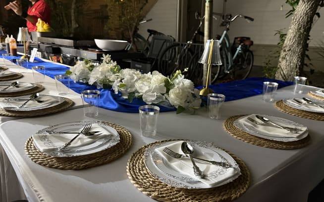 Courtyard table laid with white florals, chargers and cutlery, bicycles parked against the wall behind