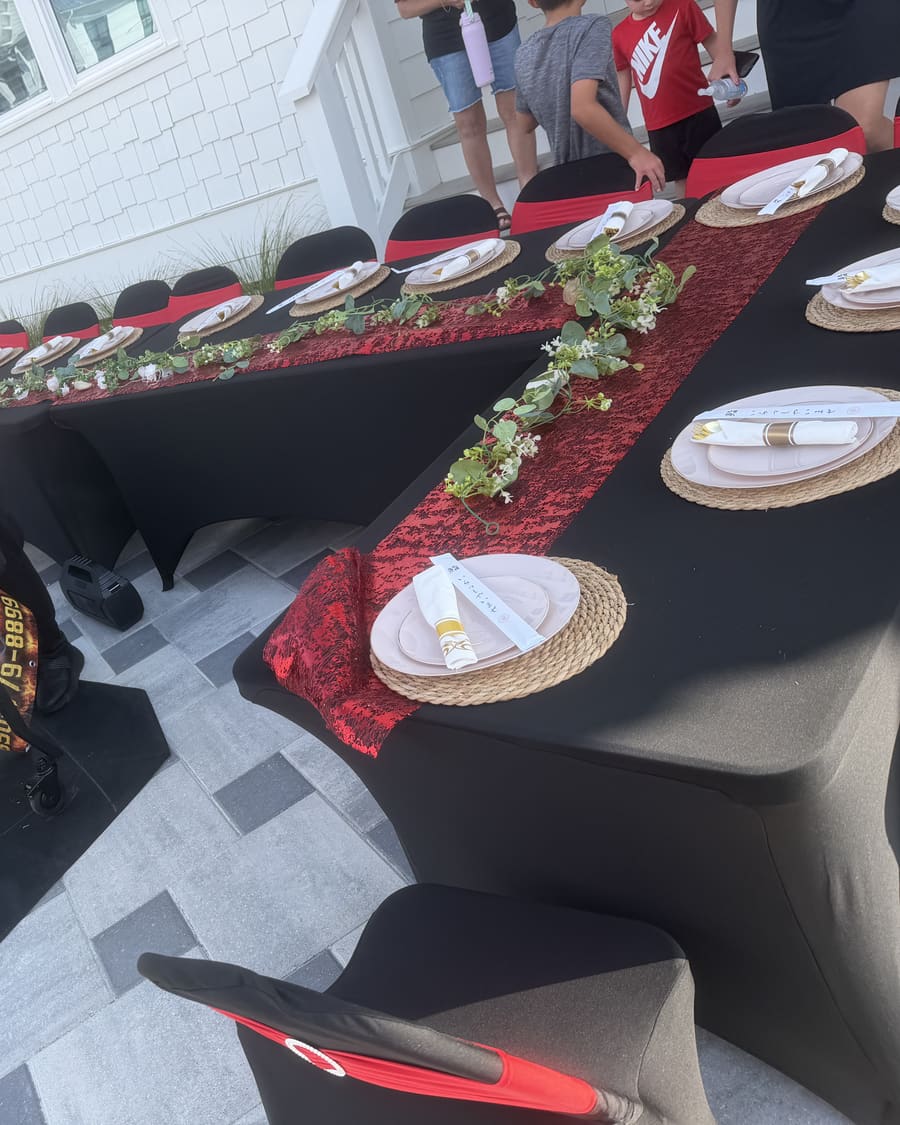 Chef working the flat-top beside a long table with a red runner outside a white clapboard rental house