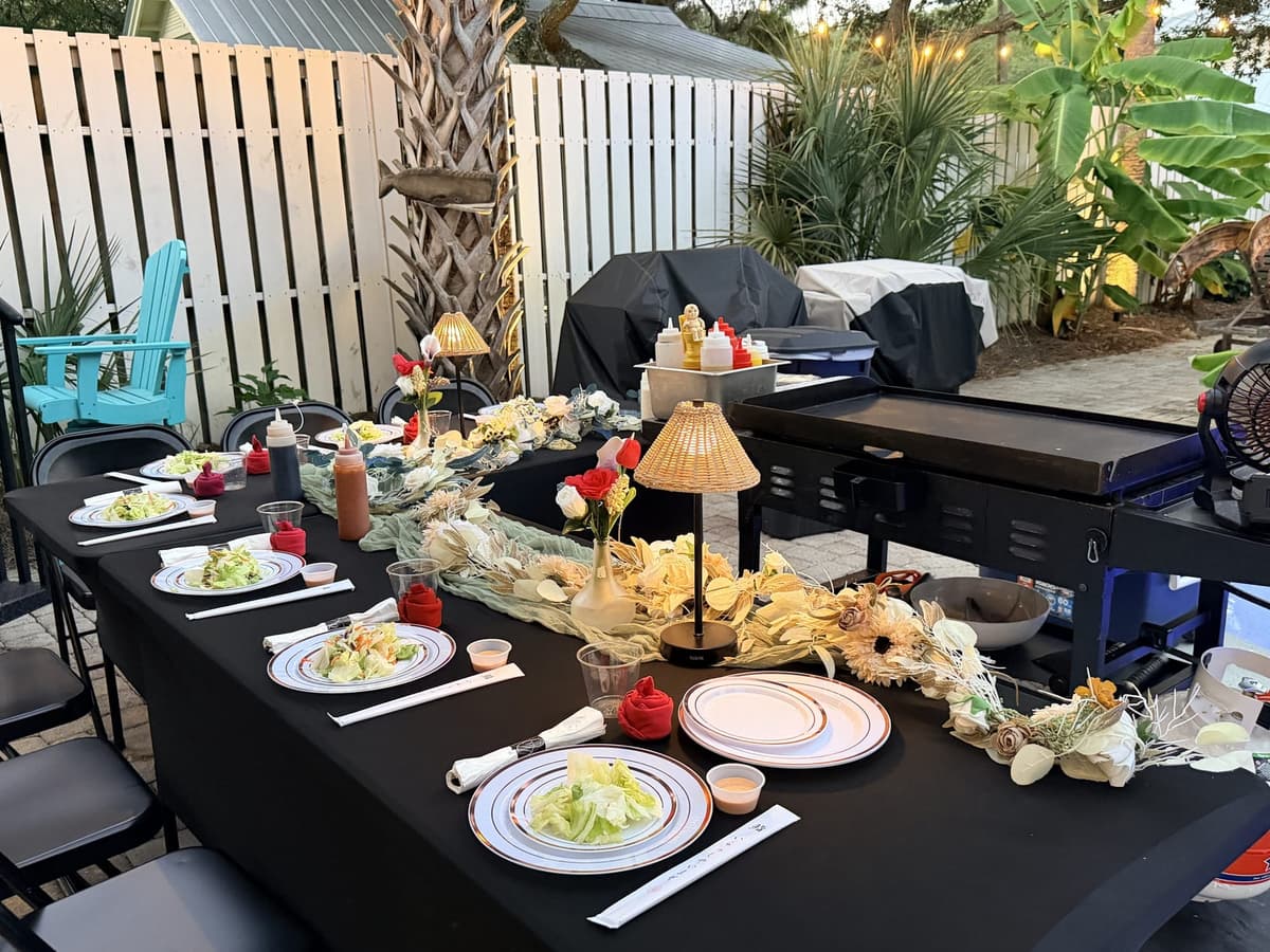 A long table dressed in black with shaded lamps and plated salads down its length, set out on a paved terrace at dusk