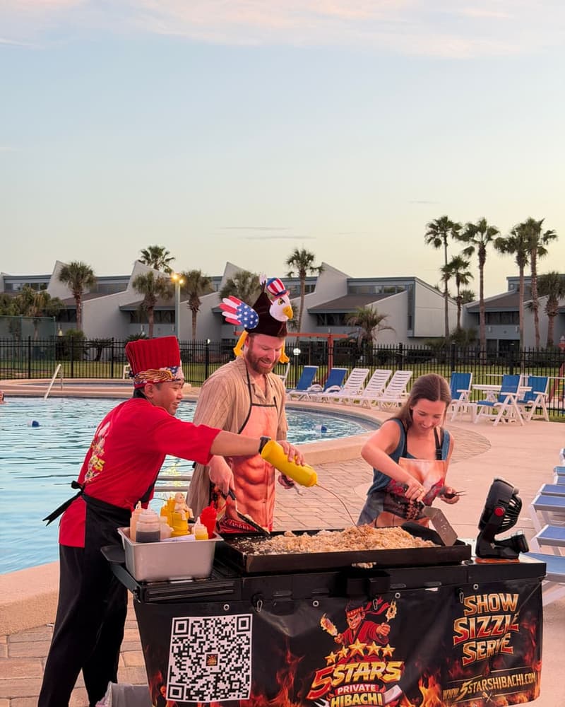 Chef cooking on the flat-top while two guests in novelty hats watch from the poolside