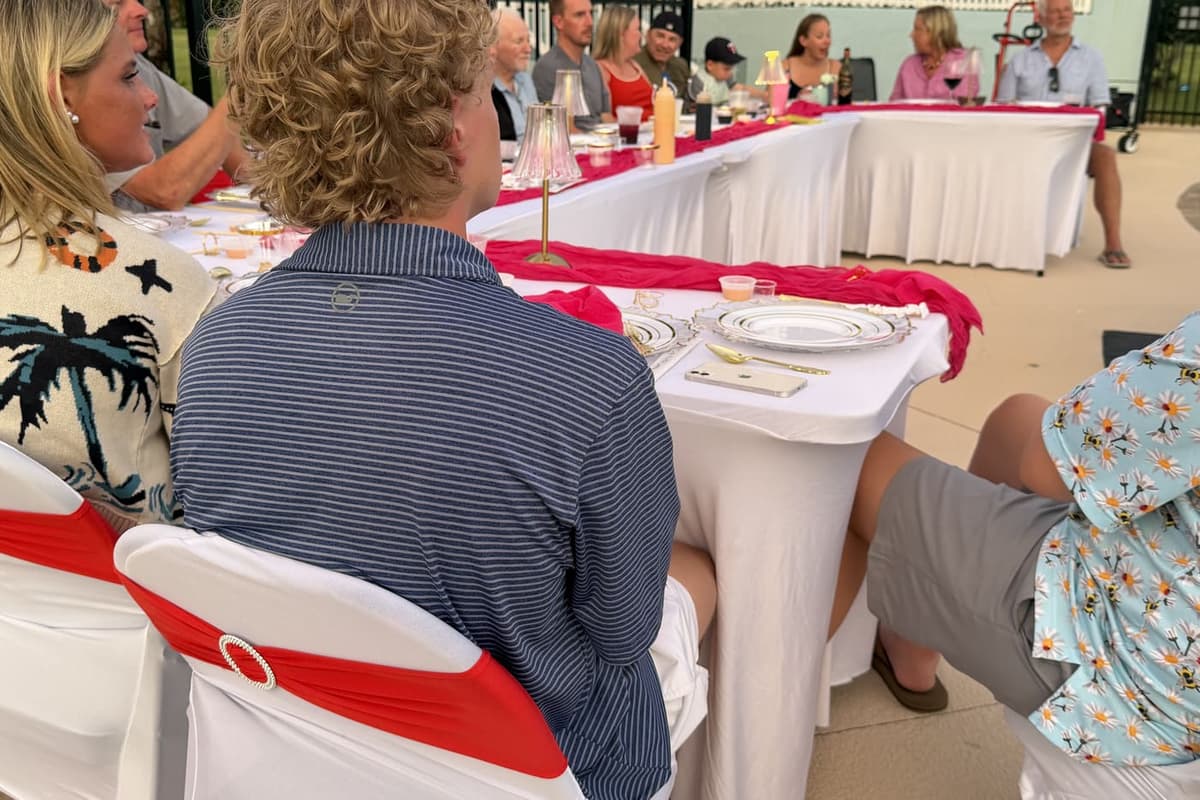 Guests seated at a long table with white linen and red runners, plates set and service underway