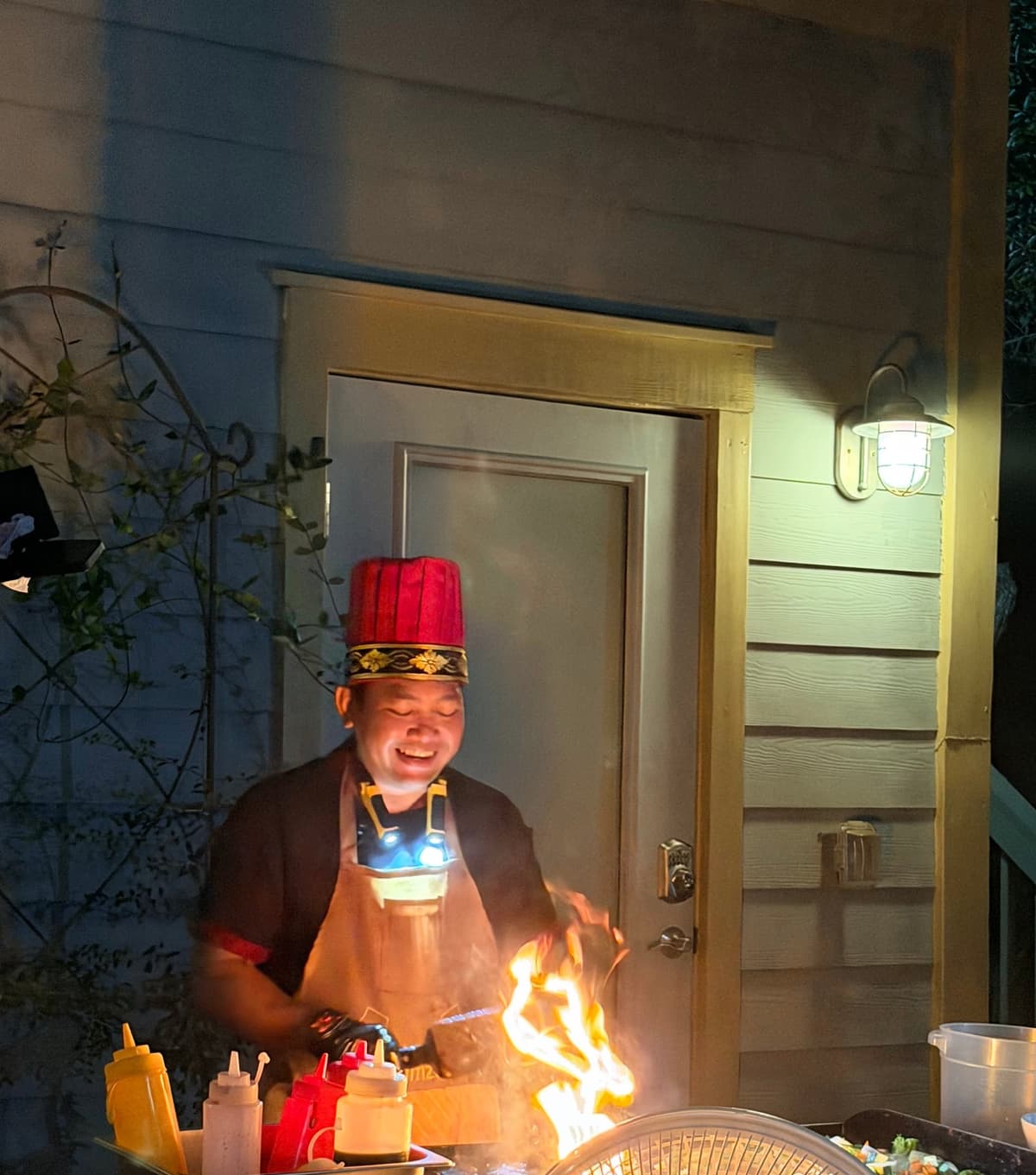 Hibachi chef in a red fez sending a column of flame up from the flat-top beside the back door of a 30A rental at night